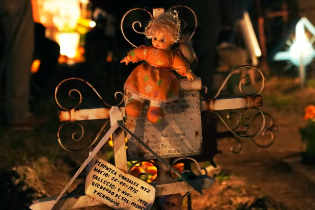 A doll decorates a newborn's tomb at the San Gregorio Atlapulco cemetery during Day of the Dead festivities on the outskirts of Mexico City, Wednesday, early Nov. 1, 2023. In a tradition that coincides with All Saints Day on Nov. 1 and All Souls Day on Nov. 2, families decorate graves with flowers and candles and spend the night in the cemetery, eating and drinking as they keep company with their dearly departed. (AP Photo/Marco Ugarte)