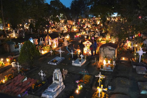 People gather in the section of children's tombs inside the San Gregorio Atlapulco cemetery during Day of the Dead festivities on the outskirts of Mexico City, early Wednesday, Nov. 1, 2023. In a tradition that coincides with All Saints Day on Nov. 1 and All Souls Day on Nov. 2, families decorate graves with flowers and candles and spend the night in the cemetery, eating and drinking as they keep company with their dearly departed. (AP Photo/Marco Ugarte)