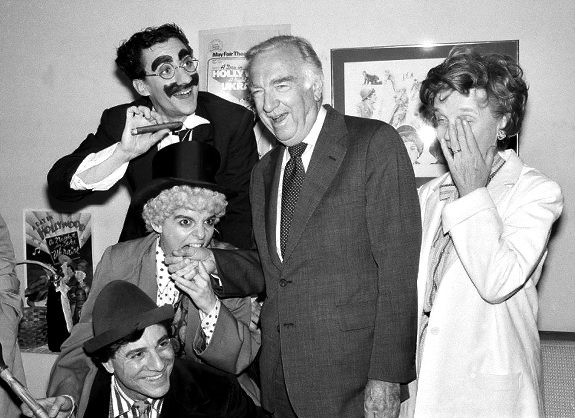 Walter Cronkite, second from right, has his hand bitten by actress Priscilla Lopez who plays Harpo Marx in the Broadway comedy 