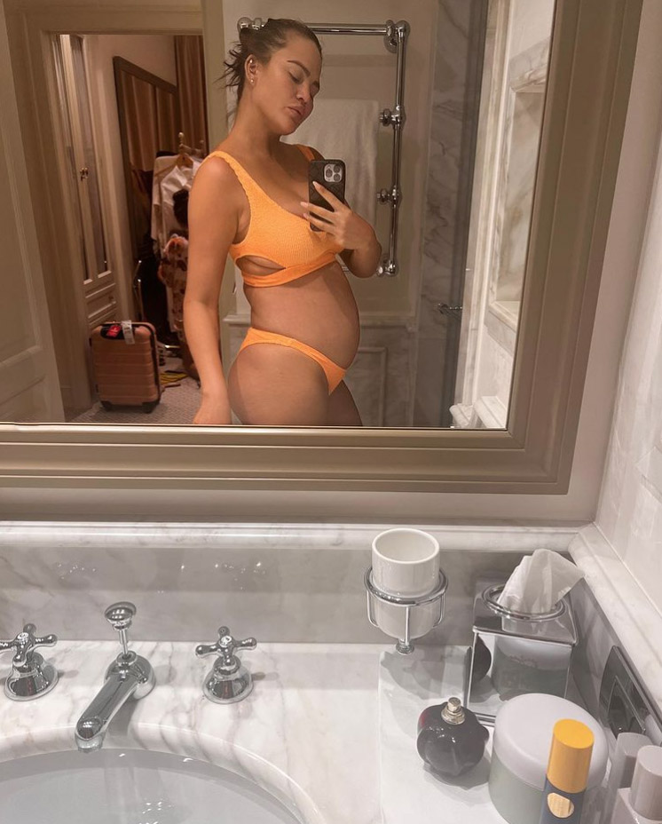 Chrissy Teigen shows off her growing baby bump while rocking a bright orange bikini on Monday, Aug. 22, 2022.